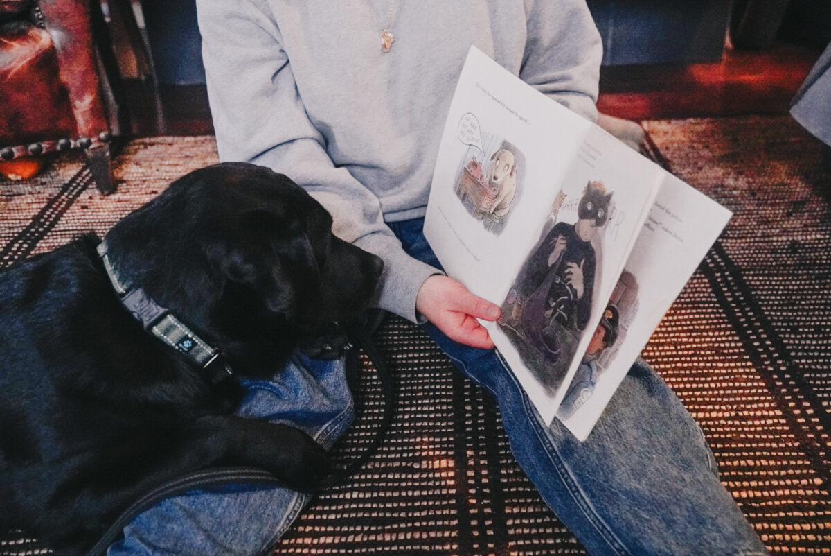 Photo: A black lab listens to a picture book being read to her